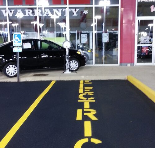A black car parked in the lot of an electric vehicle dealership.